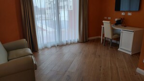 A room with a wooden floor, a desk with a chair, a television mounted on the wall, and a window with curtains. - RMaison Luxury Suites Olbia  (Olbia)