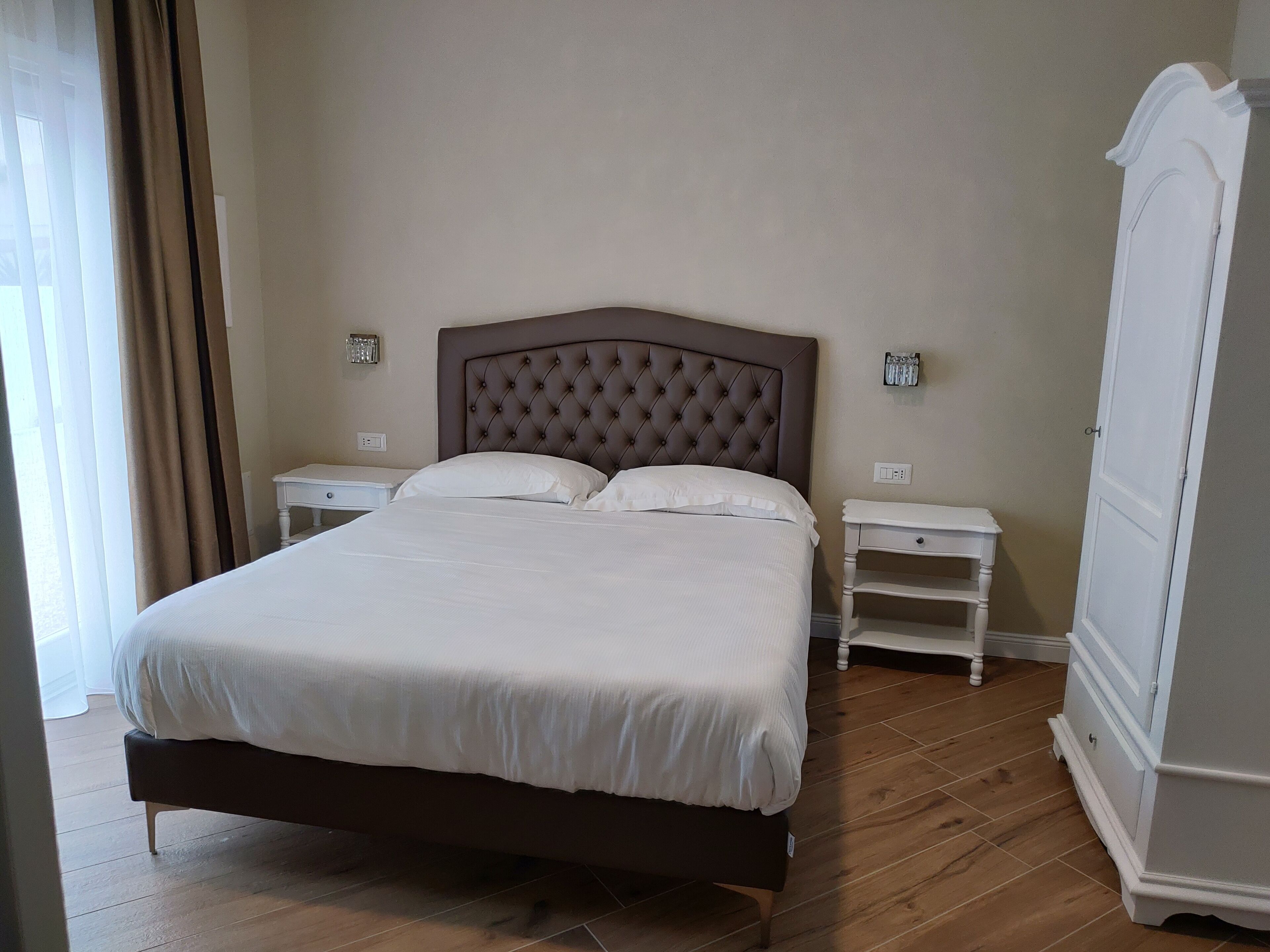 A neatly made bed with a tufted headboard, two bedside tables, and a wardrobe.