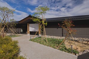 A traditional Japanese building with a gravel path leading to the entrance, surrounded by small trees and shrubs. - HITOTSU NOTOJIMA (Nanao)