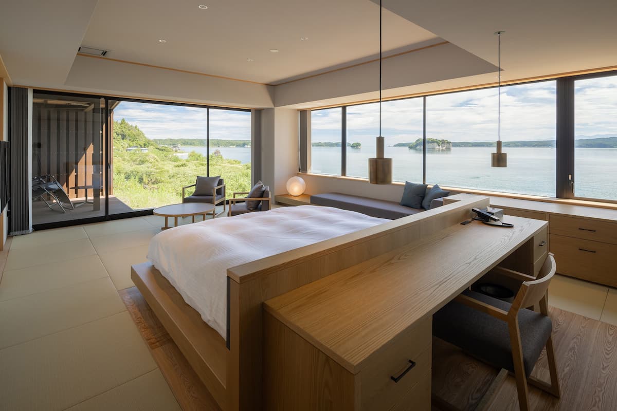 A modern bedroom with a large bed, a desk, and a view of a lake.