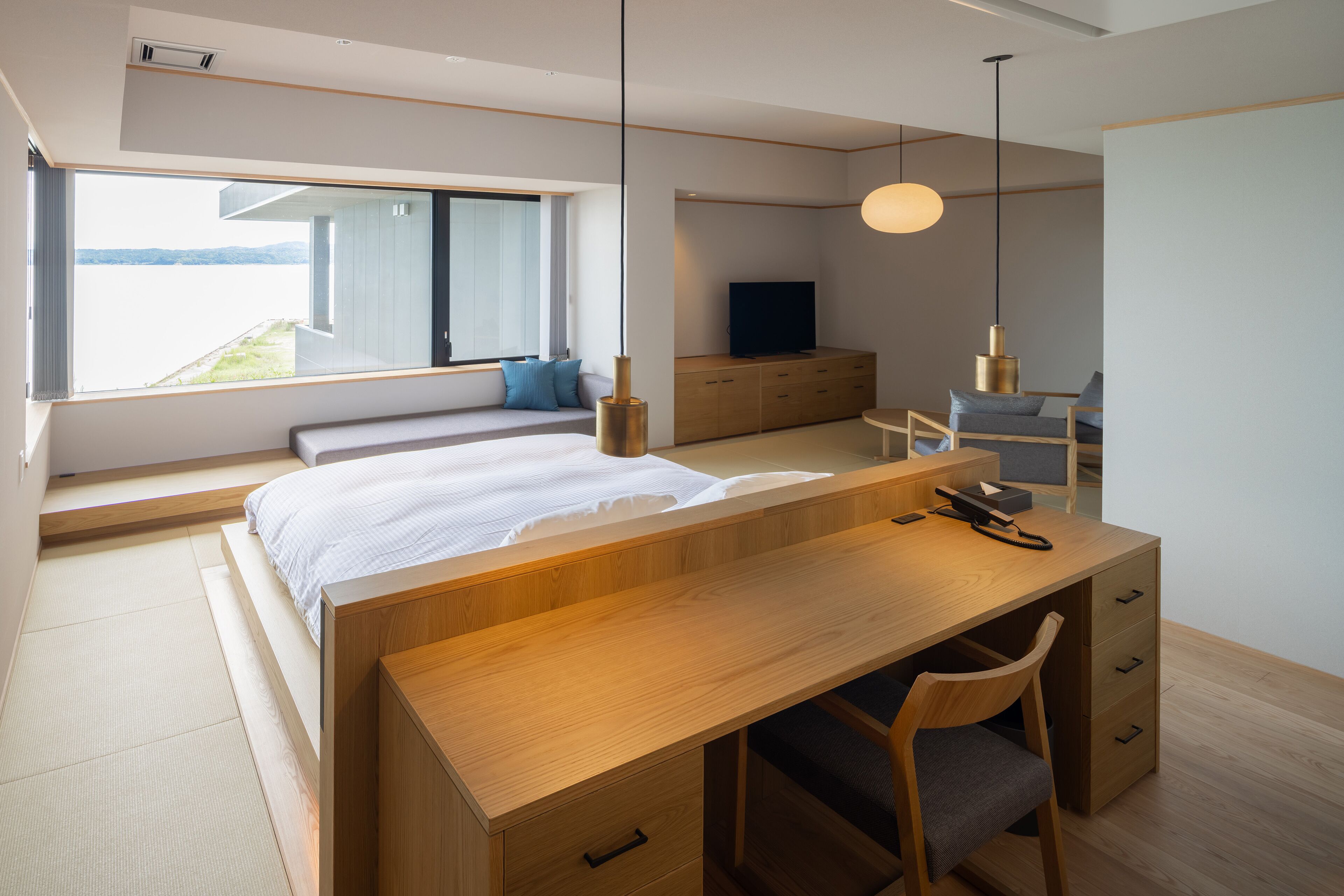A modern bedroom with a large bed, wooden desk, and a view of the outdoors.