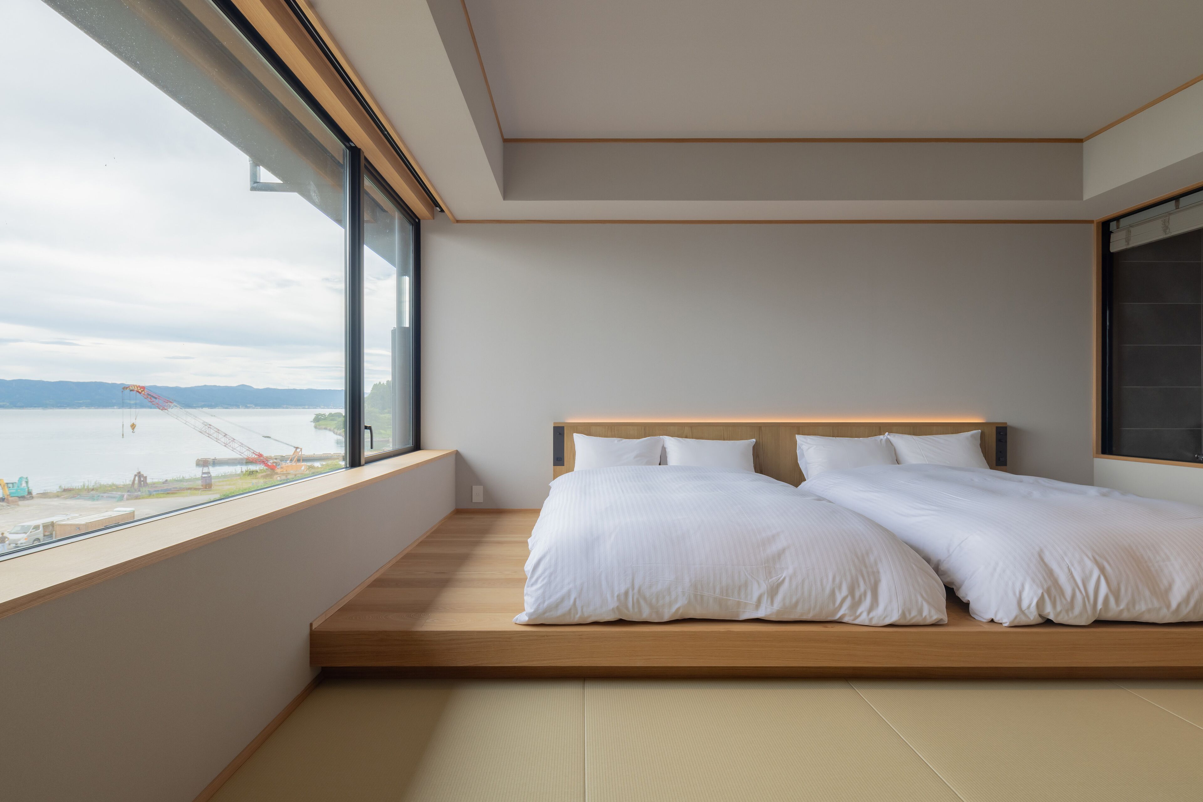 Un dormitorio con un amplio ventanal que da a una masa de agua y una zona de construcción.