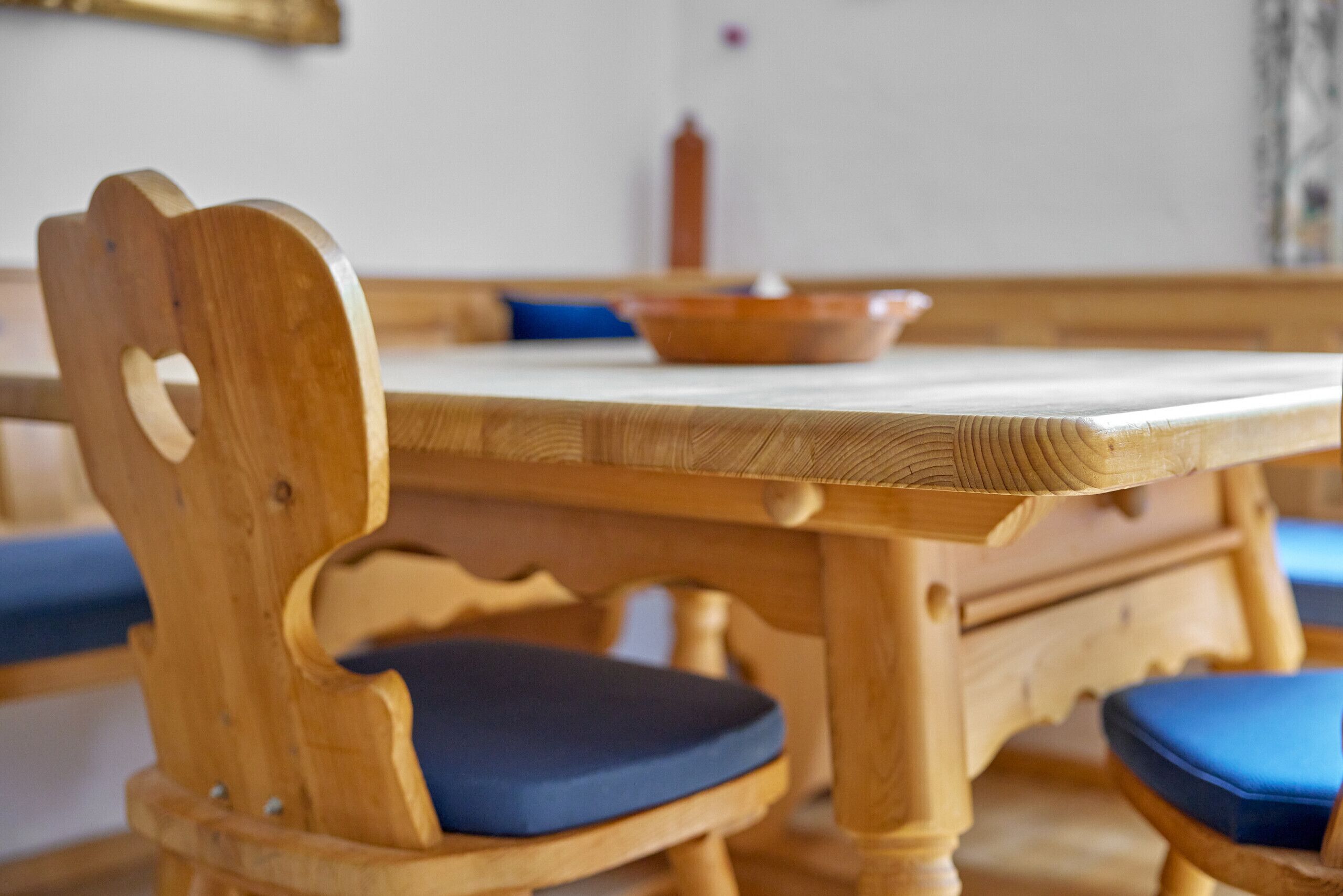 A wooden dining table with a blue cushion, a wooden chair with a blue cushion, and a bowl on the table.