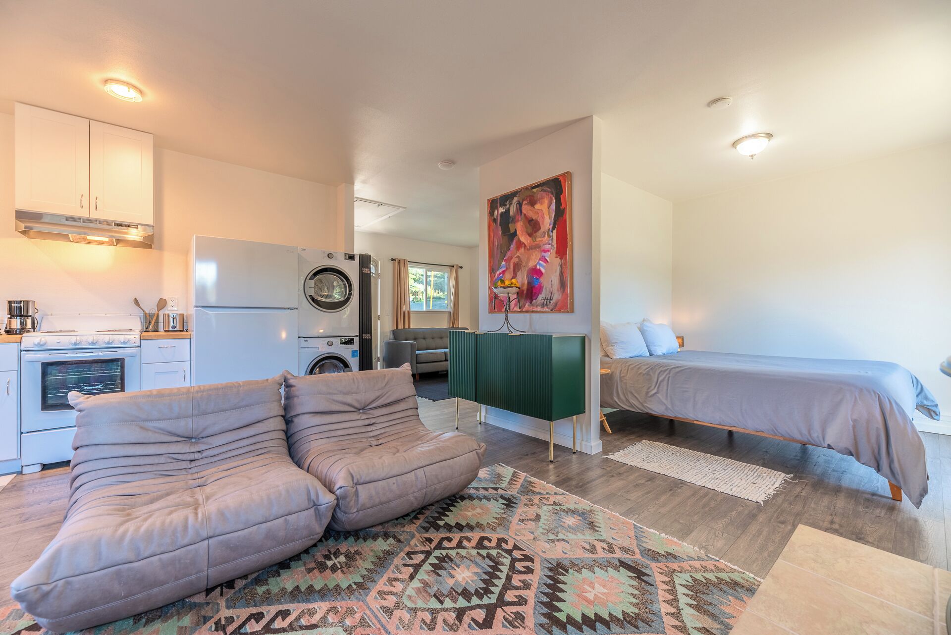 A compact living space with a kitchenette, a sofa, a bed, and a colorful rug.