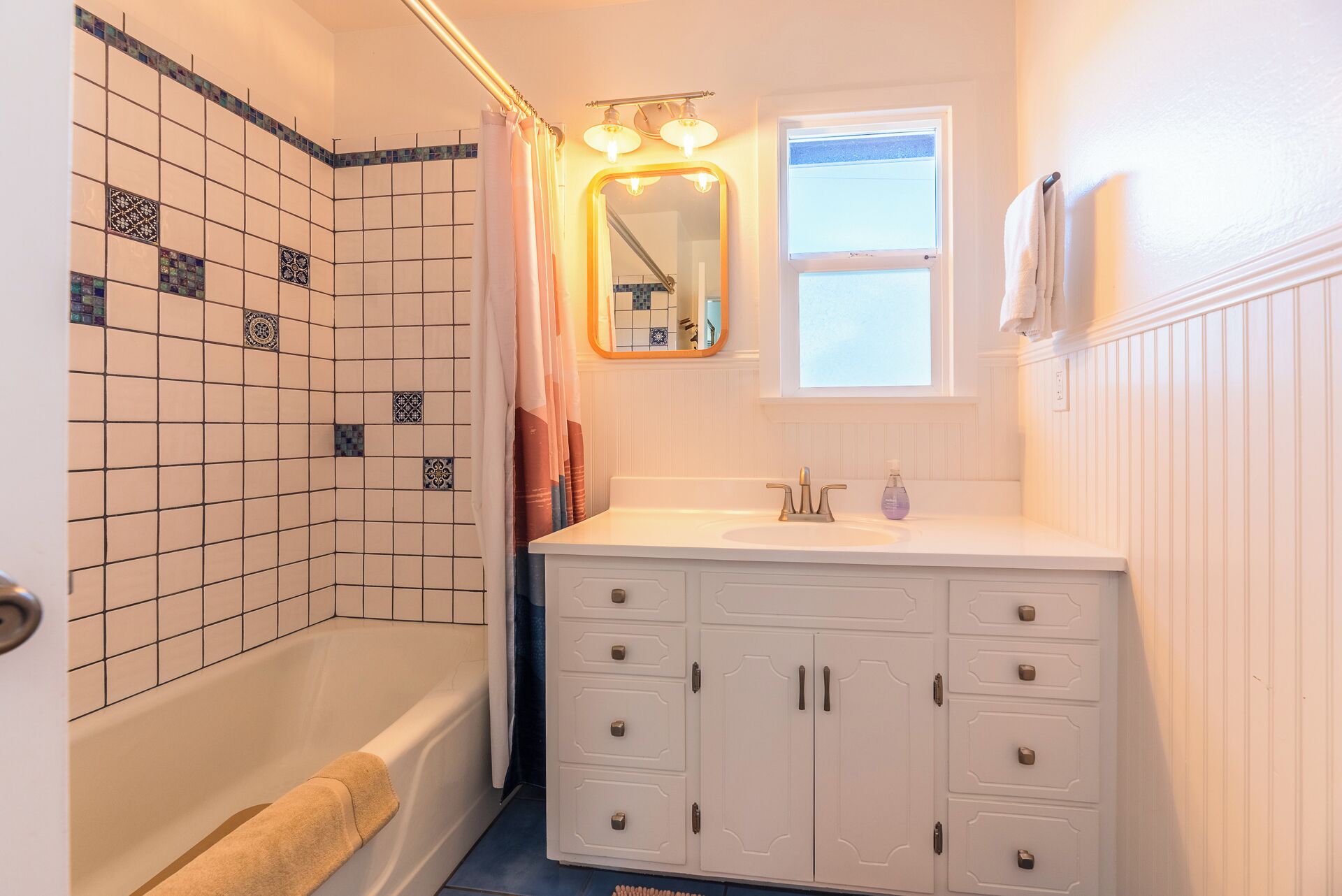 A bathroom with a bathtub, a white sink with a mirror above it, and a window.