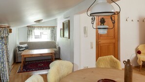 A cozy living room with a sofa, a wooden table, and a fluffy chair. There's a wooden door and a window with curtains. - 1302 Alt Montafon Appartment 2 (Gaschurn)