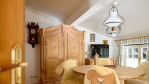 A dining area with a wooden table and chairs, a wooden cabinet, a clock, and a television. - 1302 Alt Montafon Appartment 2 (Gaschurn)