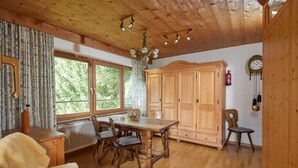 Une salle à manger en bois, avec une grande table et des chaises, un lustre et une vue sur la verdure à l’extérieur.