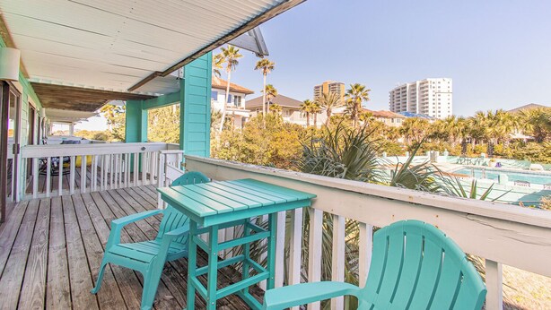 Une terrasse en bois avec des chaises turquoise et une table, donnant sur une piscine et des palmiers.