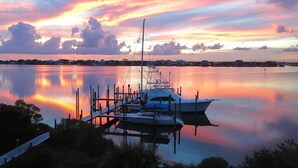 Un port de plaisance où des bateaux sont amarrés à des quais en bois, une eau calme qui reflète le ciel et une côte lointaine.