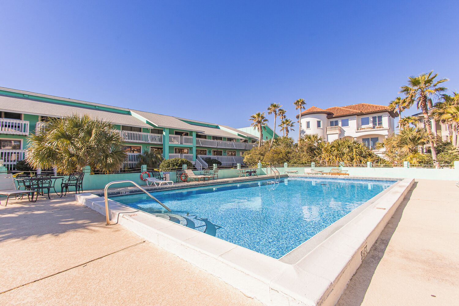 A hotel with a swimming pool, outdoor seating, and palm trees.