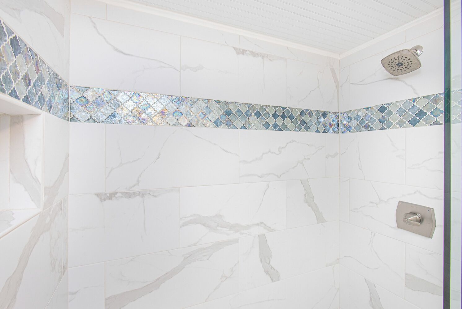 A bathroom with white marble walls and a decorative mosaic tile border.