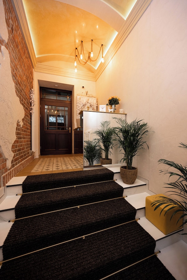 Um hall de hotel moderno com parede de tijolos, porta de madeira e escadaria que leva ao andar superior.