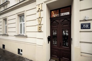 A building with a large sign reading "HIVE" on the facade, a dark wooden door with glass panels, and a street sign indicating the address "Aleja Mickiewicza 59, Dzw. IV, Piaszek." - Hive Family House (Kraków)