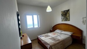 Une chambre à coucher avec un lit, une table de chevet, une fenêtre et un tableau accroché au mur.