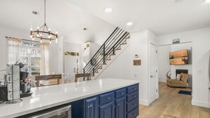 A modern kitchen with a central island, a staircase with black railings, and a dining area with white chairs. - Private Pool | 6-Seater LSV | Garage (Santa Rosa Beach)