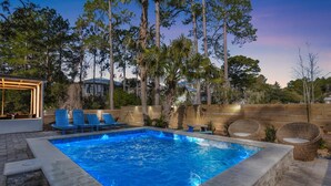 A rectangular swimming pool with blue tiles, surrounded by stone steps and wooden deck. There are blue lounge chairs and wicker chairs around the pool. - Private Pool | 6-Seater LSV | Garage (Santa Rosa Beach)
