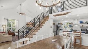 A spacious living area with a wooden dining table, white chairs, and a staircase leading to an upper level. - Private Pool | 6-Seater LSV | Garage (Santa Rosa Beach)
