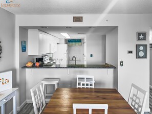 A modern kitchen with white cabinets, a wooden dining table, and a view into the adjacent living area.