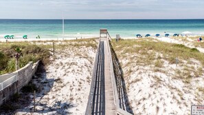 A beach with a wooden boardwalk leading to the water, surrounded by sand dunes and beach umbrellas.