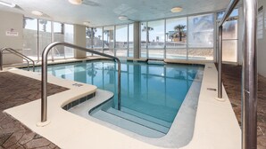Una piscina interior con paredes de vidrio transparente, suelo de baldosas y barandillas de metal.