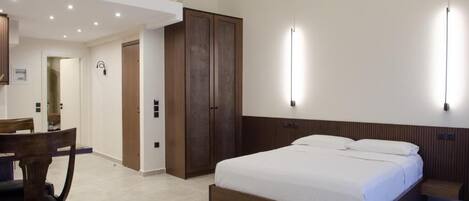 A hotel room with a bed, a wooden wardrobe, a desk with a chair, and a mirror.