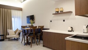 A modern kitchen with a central island, a dining area with chairs, a sofa, and a TV mounted on the wall. - Leone Suites (Nafpaktos)