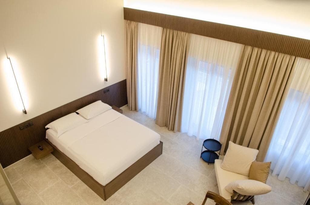 Una habitación de hotel con una cama grande, un sofá pequeño, un set de batería y un ventanal con cortinas.