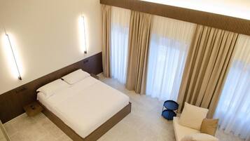 Una habitación de hotel con una cama grande, un sofá pequeño, un set de batería y un ventanal con cortinas.