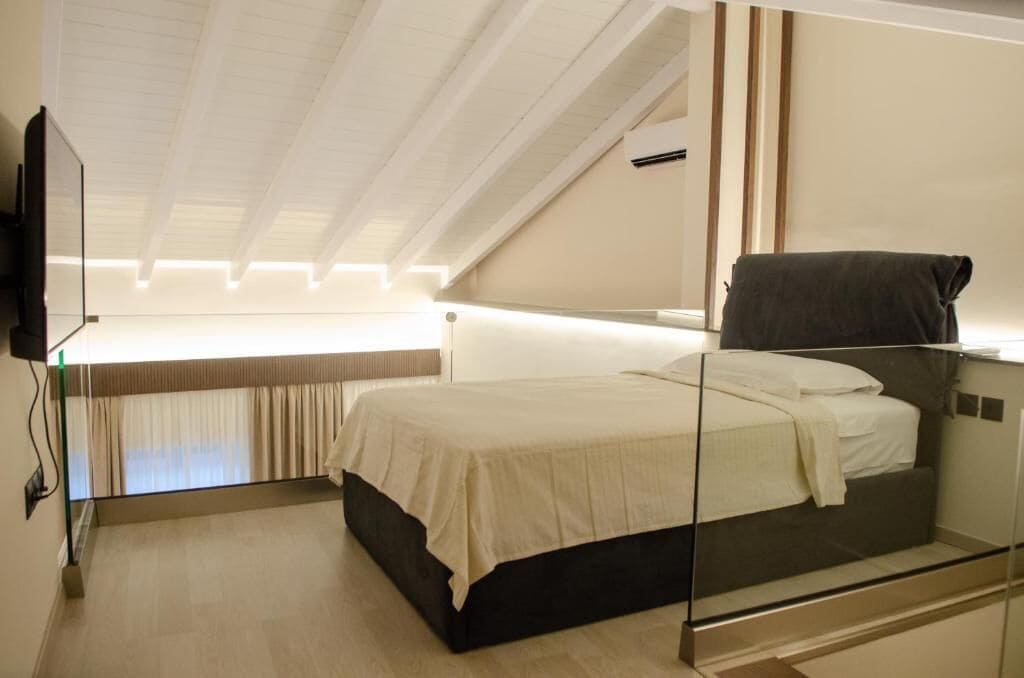 Een moderne slaapkamer met een glazen bed, een flatscreen televisie aan de muur en een plafond met zichtbare balken.