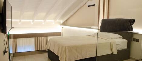 Un dormitorio moderno con una cama de cristal, un televisor de pantalla plana montado en la pared y un techo con vigas a la vista.