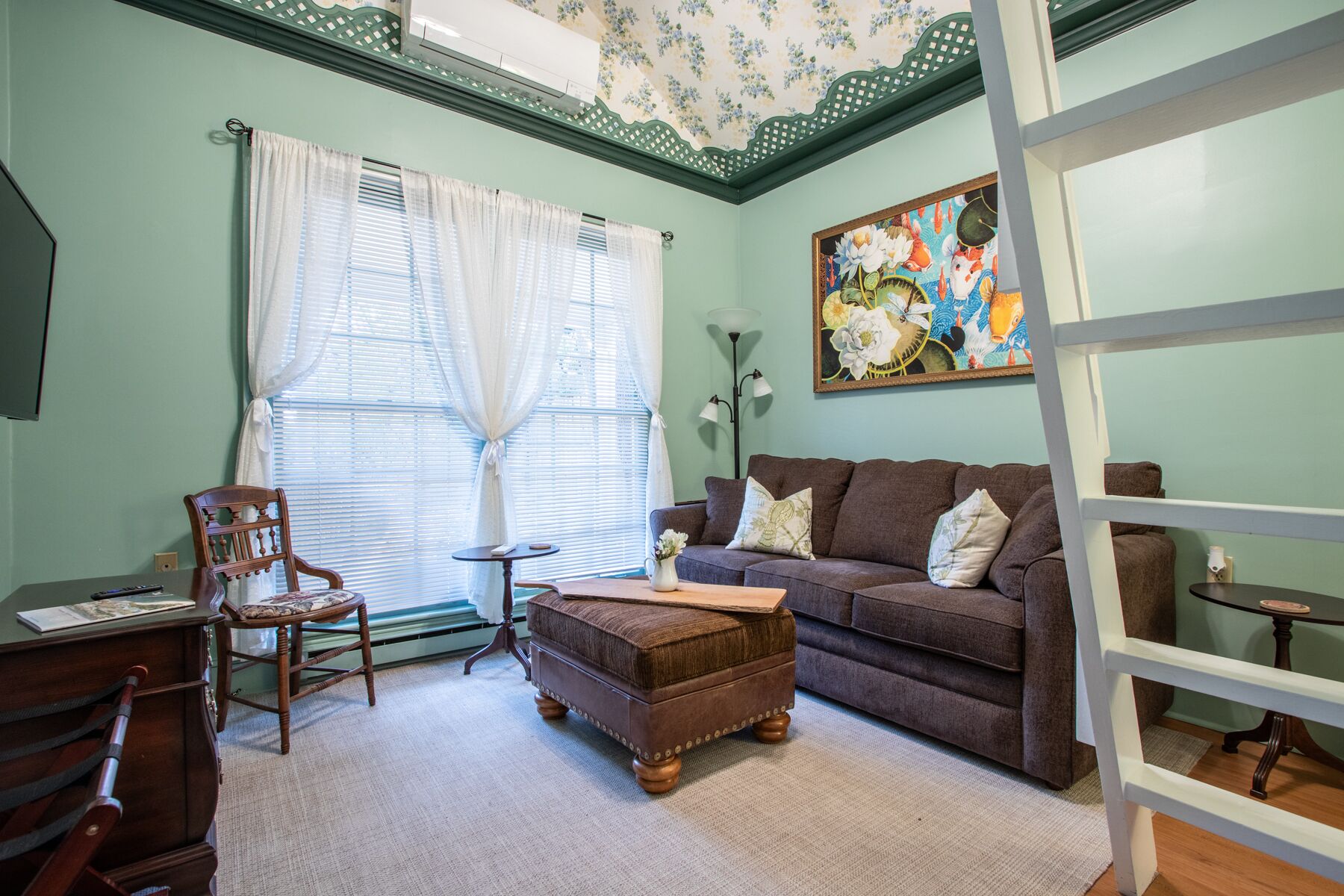 A living room with a brown sofa, a wooden chair, a small table, and a painting on the wall.