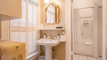 A bathroom with a pedestal sink, a large mirror, and a shower area.