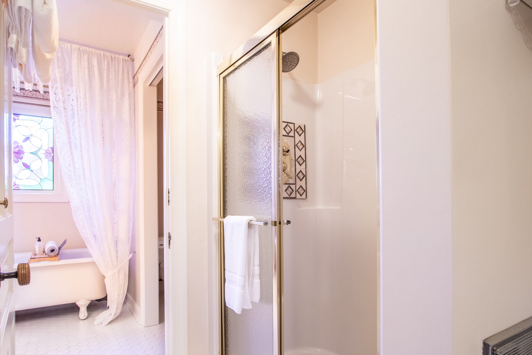 Un baño con mampara de vidrio, bañera blanca y ventanal con estampado floral.