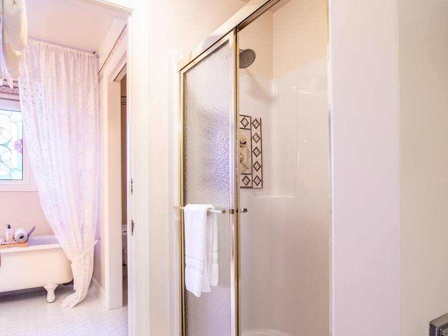 Un baño con mampara de vidrio, bañera blanca y ventanal con estampado floral.