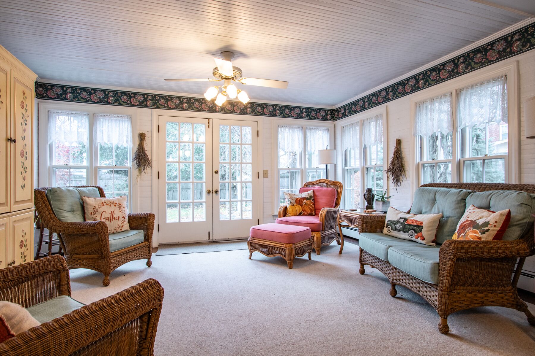A cozy room with wicker furniture, a ceiling fan, and large windows.