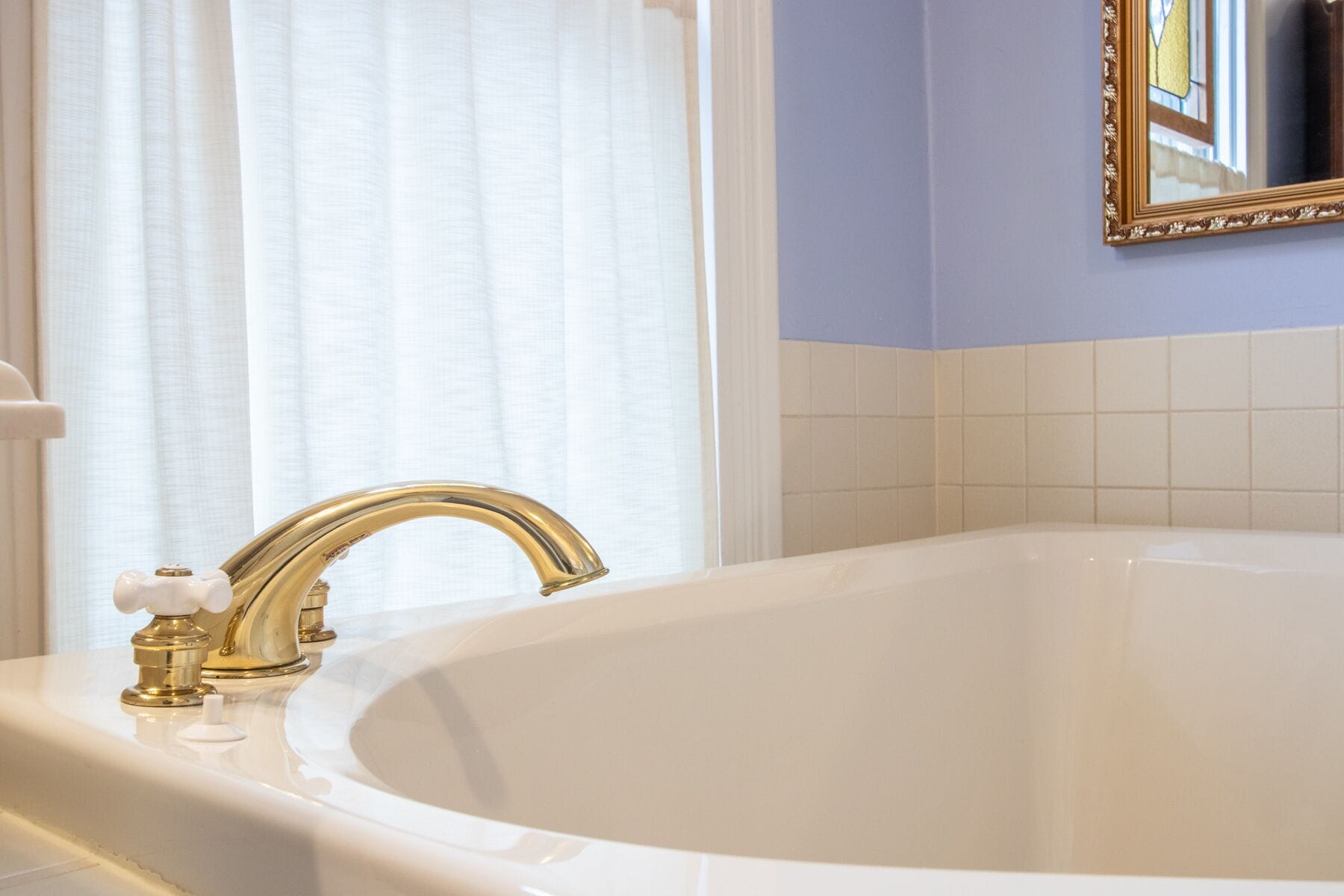 A bathroom with a white bathtub, a gold faucet, and a mirror with a gold frame.