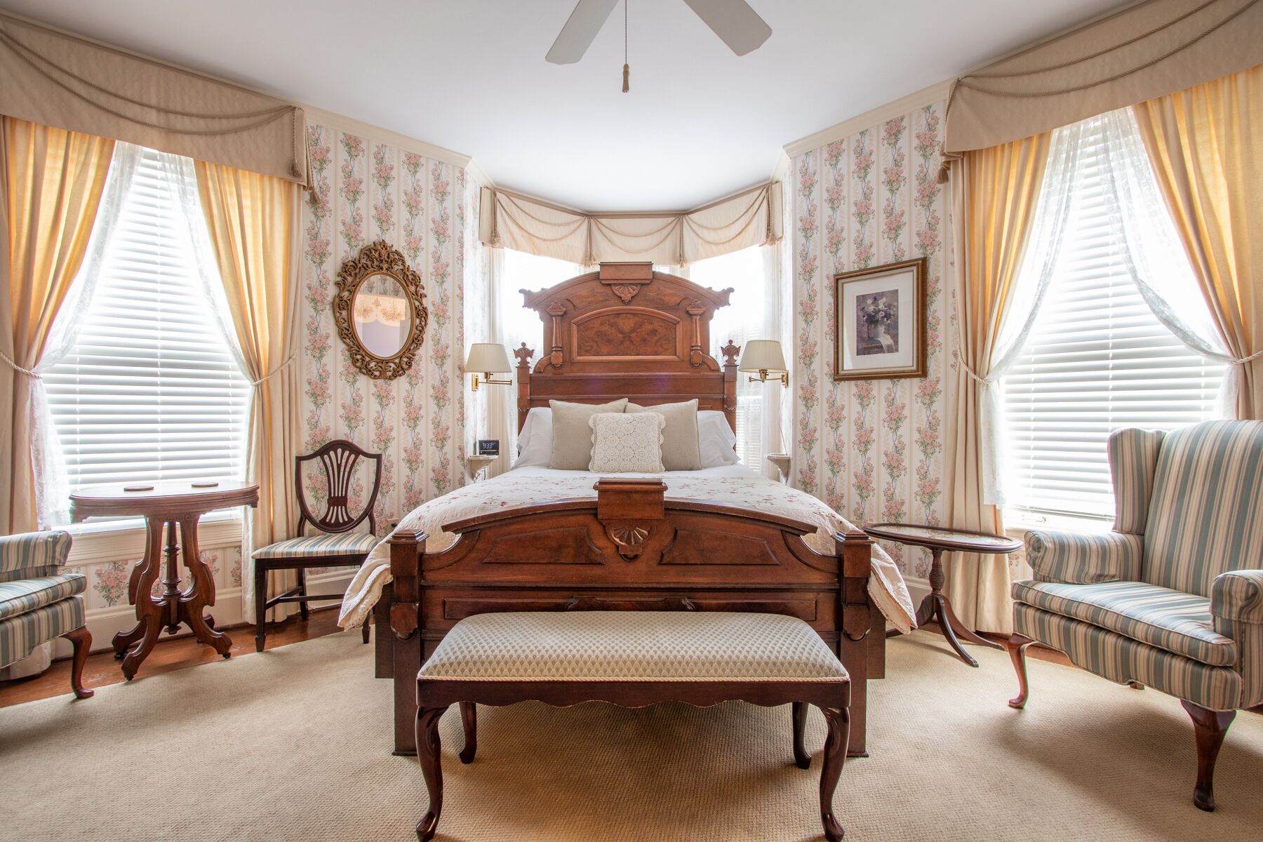 A classic bedroom with a large wooden bed, two upholstered chairs, a small table, and a bench.