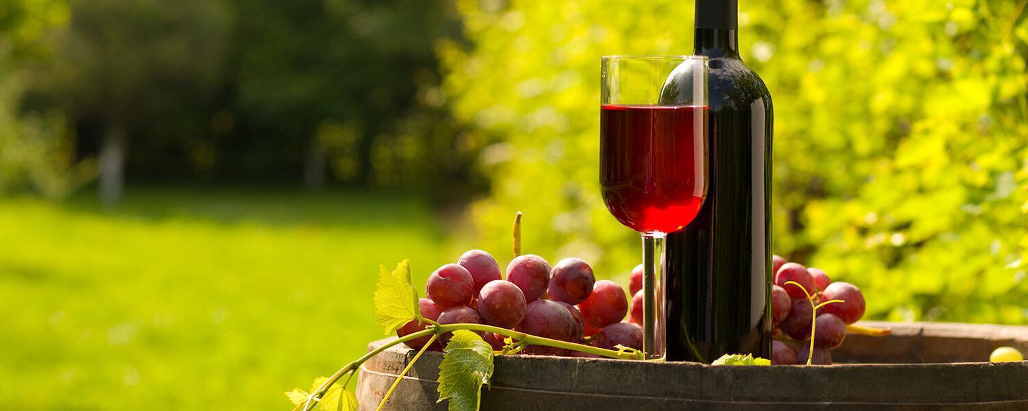 A wine bottle and glass on a wooden surface with grapes and leaves.