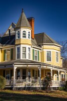 Una casa grande de estilo victoriano, de color amarillo, con una torreta destacada y un porche que rodea toda la estructura.
