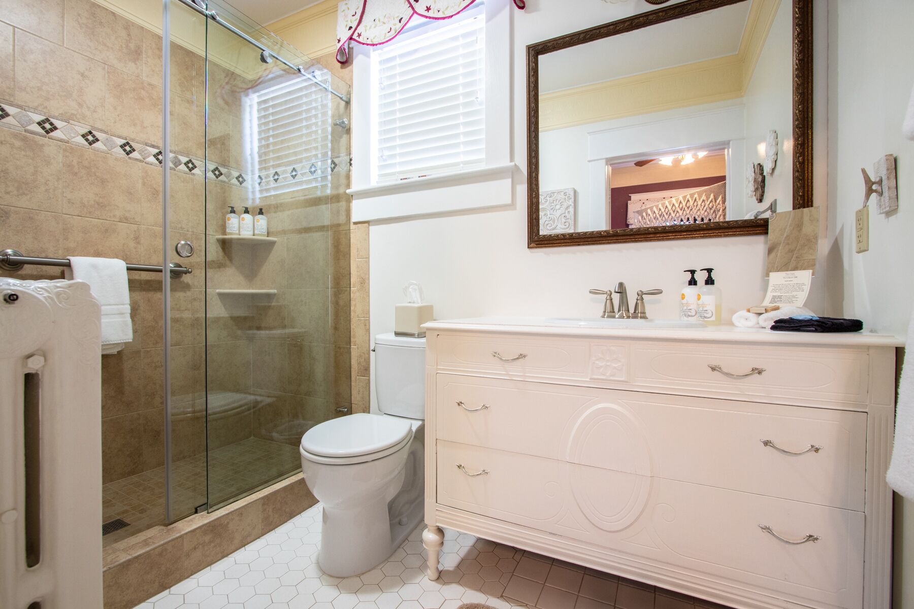 A bathroom with a glass-enclosed shower, a white toilet, and a vanity with drawers and a mirror.