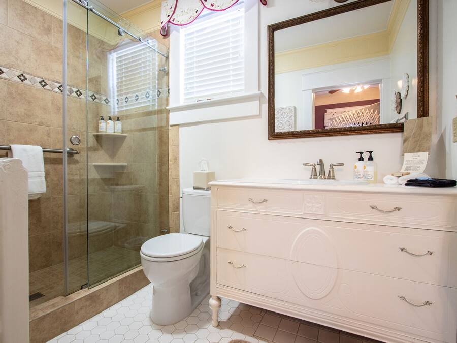 A bathroom with a glass-enclosed shower, a white toilet, and a vanity with drawers and a mirror.