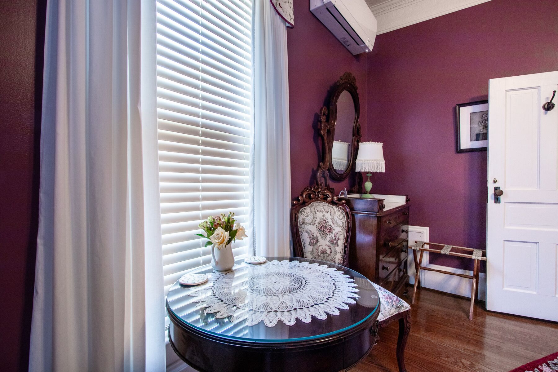 A room with a round glass table, a chair, a mirror, and a door.