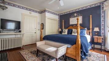 A bedroom with a four-poster bed, a television on a stand, a radiator, a bench, and a patterned rug.