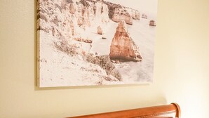 Ein Bett mit weißer Bettwäsche und einem braunen Kopfkissen, ein hölzernes Kopfteil und ein Gemälde einer Küstenlandschaft an der Wand.