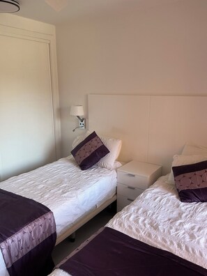 Ein Hotelzimmer mit zwei Einzelbetten, einem Nachttisch, einer Lampe und einer weißen Tür.