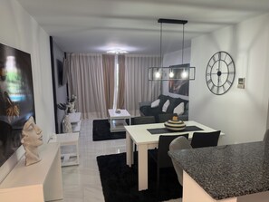 Una sala de estar moderna con comedor, un sofá blanco y negro, una mesa de centro blanca y un gran reloj de pared.