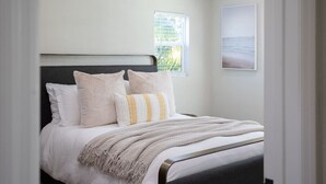 A bedroom with a bed, pillows, a blanket, a window with a view, and a framed picture on the wall.