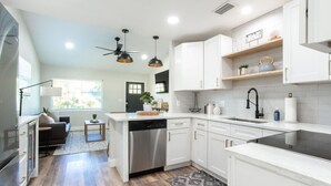 A modern kitchen with white cabinets, a dishwasher, and a black faucet. There is a window with blinds and a plant on the counter.