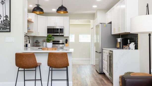 A modern kitchen with white cabinets, stainless steel appliances, and two bar stools.